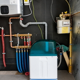 Waterontharder met blauwe en rode leidingen, geïnstalleerd naast boiler en meterkast in technische ruimte