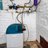 Waterontharder met filter en slangverbindingen tegen witte bakstenen muur